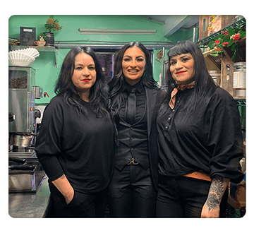 Square shaped photo of three women in all black standing in a restaurant kitchen setting
