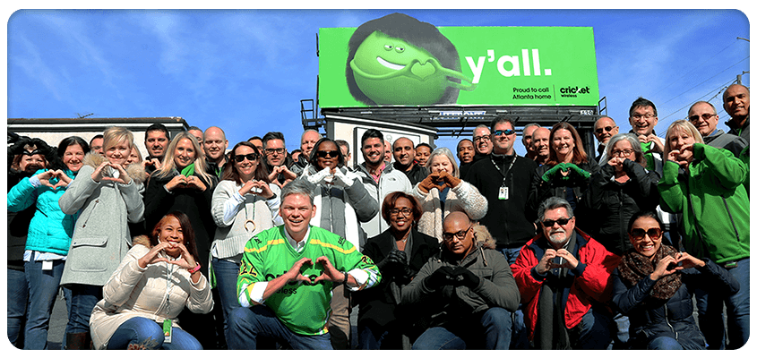 Gran foto grupal en frente de un cartel de Cricket en el que se lee "Y'all"