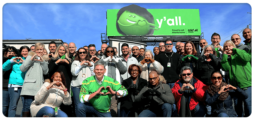 Diversidad e Inclusión: Imagen grupal para la cartelera de Cricket Gran foto grupal en frente de un cartel de Cricket en el que se lee "Y'all"
